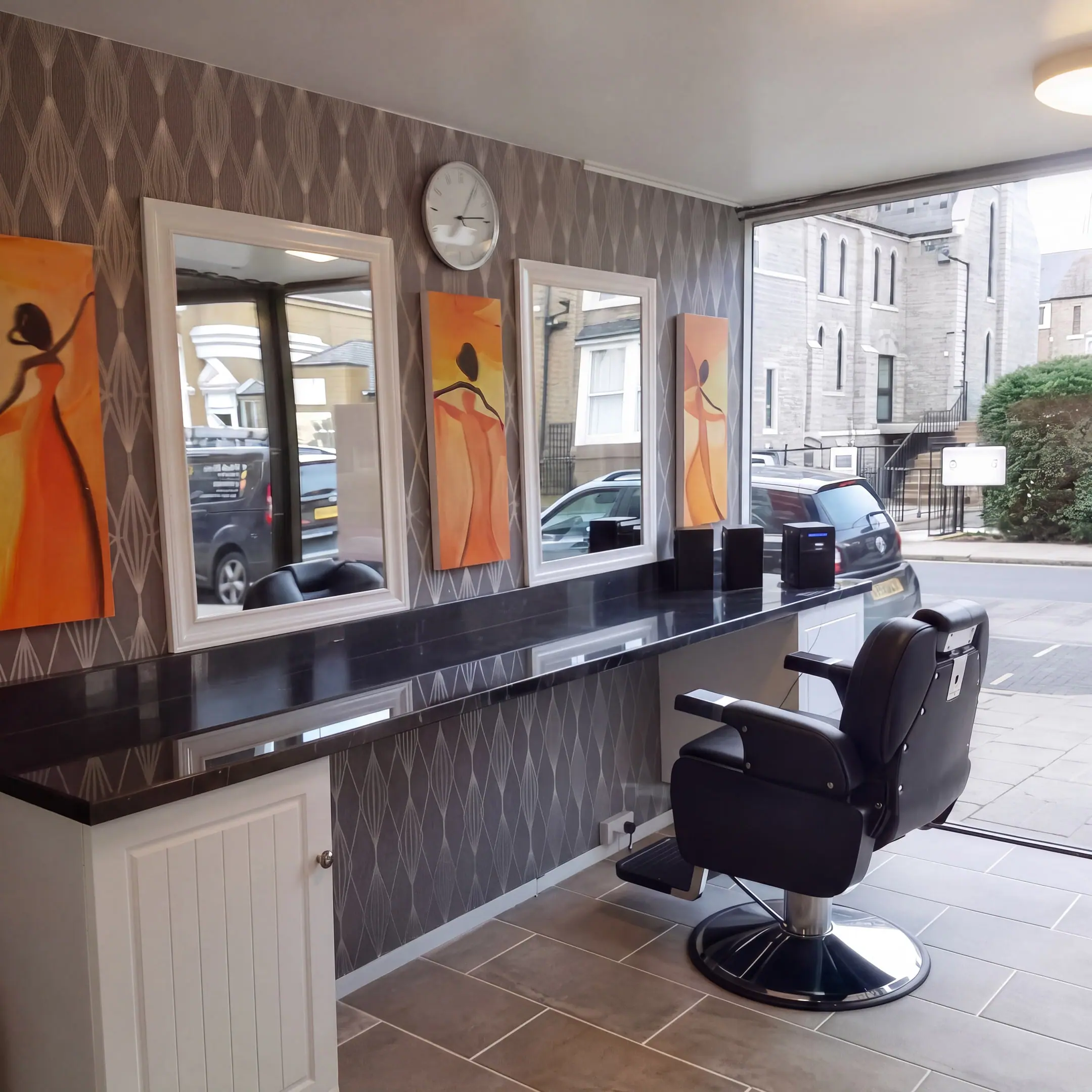 The styling station: a black granite counter with two white-framed mirrors, a wall clock and a barber chair, beside the window onto the High Street