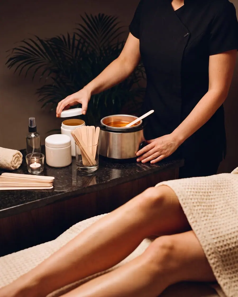 A therapist preparing a pot of warm wax at a granite counter, beside a client resting under a towel